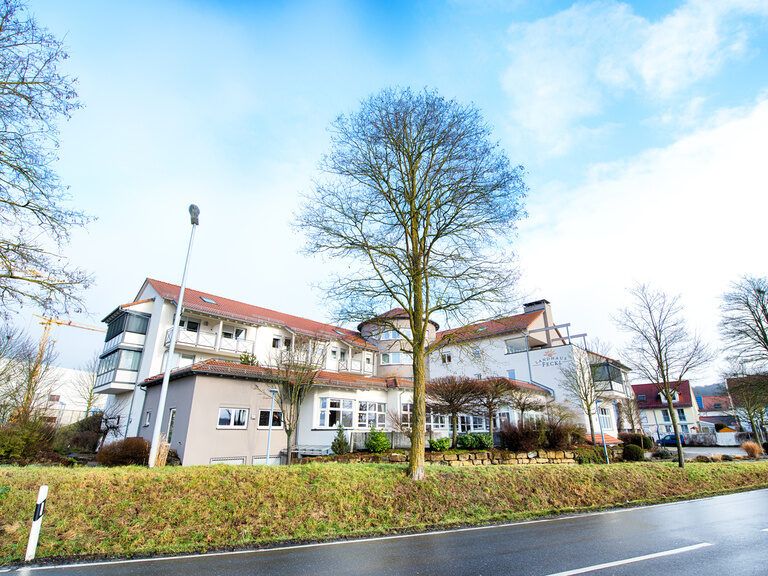 Blick auf das Landhotel Feckl im Sommer von einer Straße aus mit mehreren Bäumen.